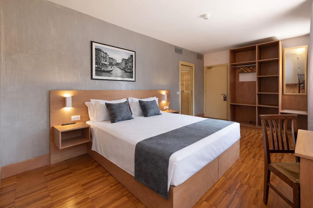 A hotel room with a large bed, bedside tables, a wardrobe, and a chair.