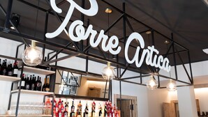 Una zona de bar con estanterías llenas de botellas y vasos, y un cartel que dice "Torre Artica".