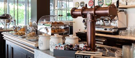A coffee station with multiple brewing options, a display of pastries, and jars of spreads.