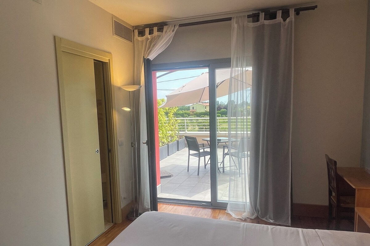 A room with a bed, a door, and a sliding glass door leading to an outdoor area with chairs and a table.