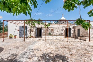 A courtyard with a pergola, stone walls, potted plants, and a building with a dome roof. - Trullo Fedele Grande125 (Ceglie Messapica)