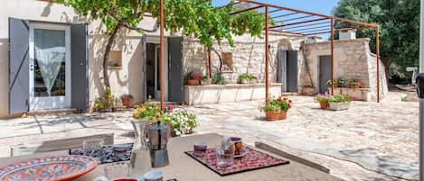 An outdoor patio with a table set for dining, surrounded by potted plants and a pergola structure.
