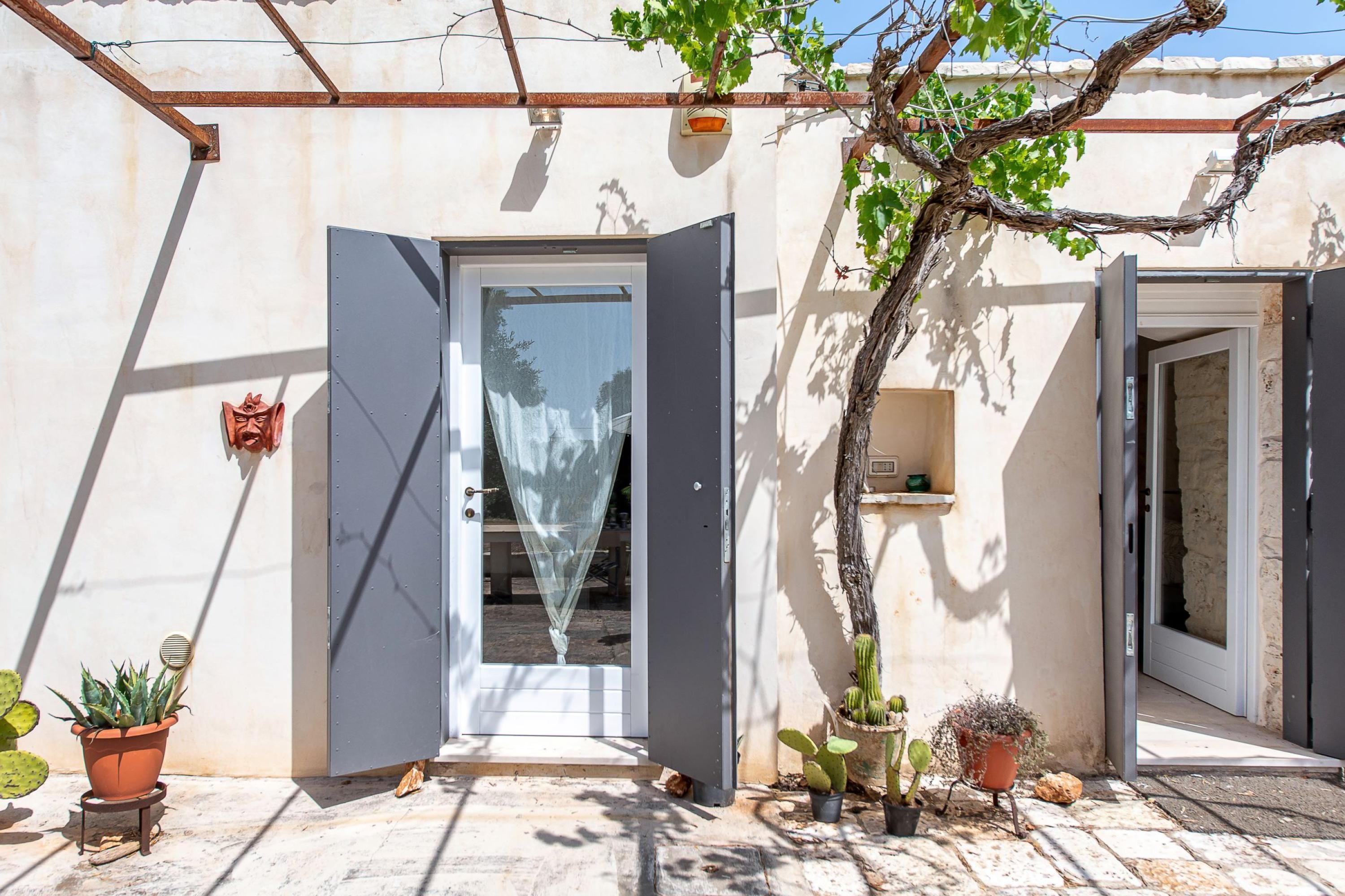 Un bâtiment avec une porte ouverte, une petite plante et un cactus en pot.