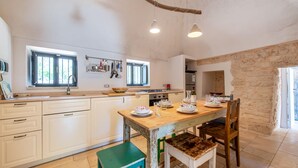 Une cuisine avec des meubles blancs, une table à manger en bois et un mur en pierre.