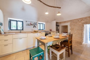 Een keuken met witte kasten, een houten eettafel en een stenen muur.