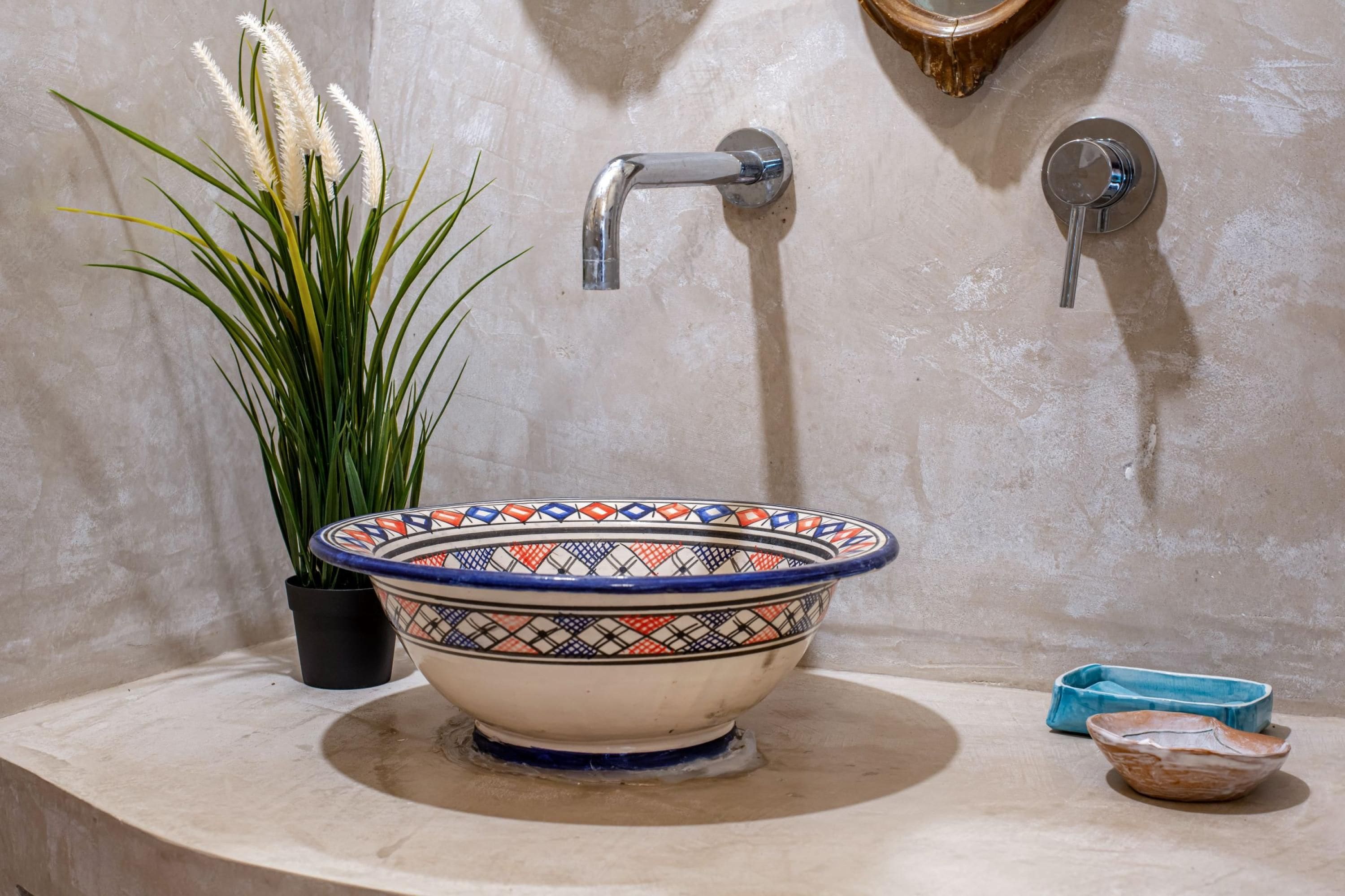 A bathroom with a decorative bowl sink, a potted plant, and a mirror.