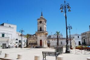 Une place carrée, avec une tour de l’horloge au centre, des bancs et des lampadaires.