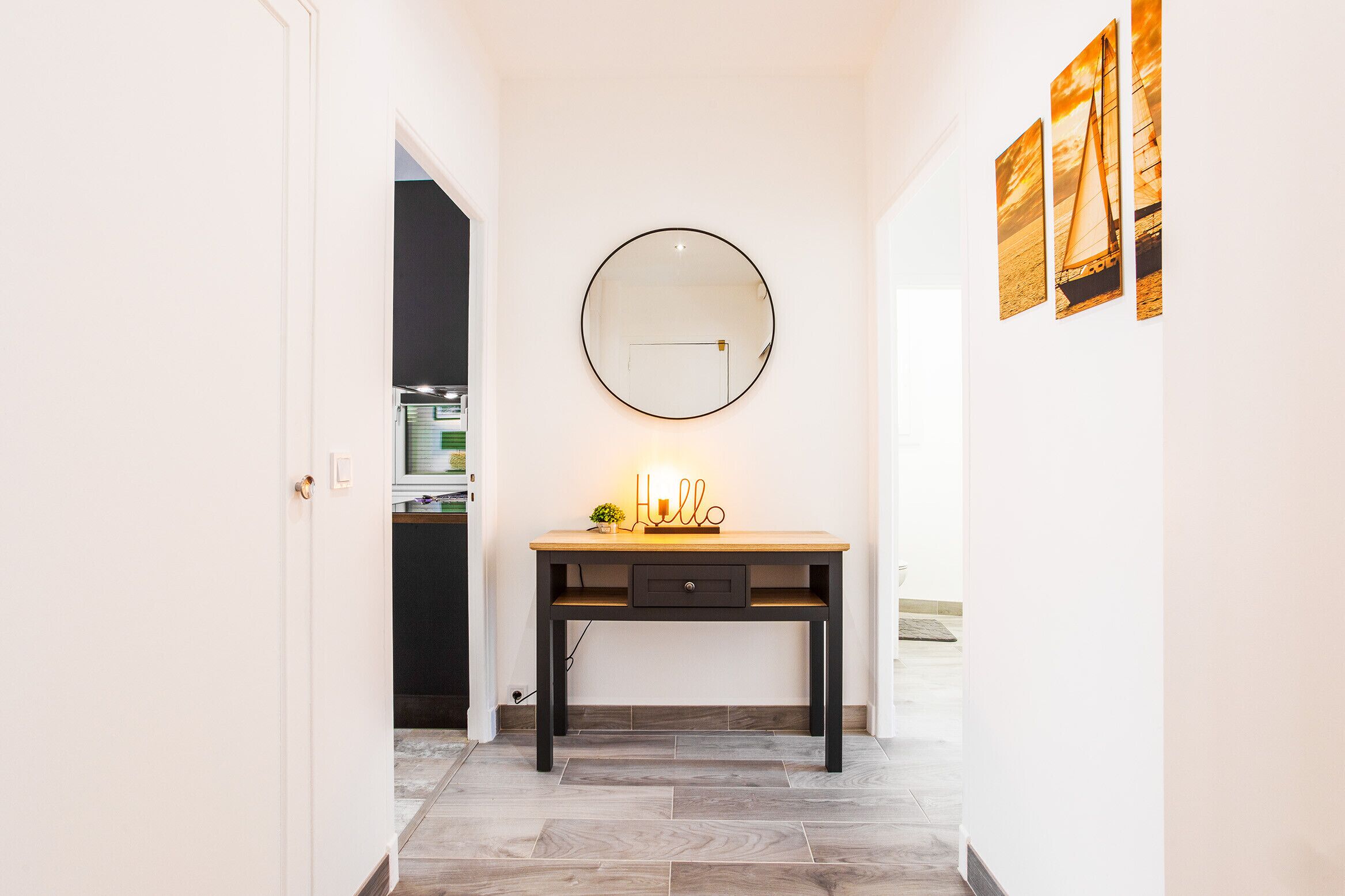 A hallway with a wooden desk, a round mirror, and a small plant.
