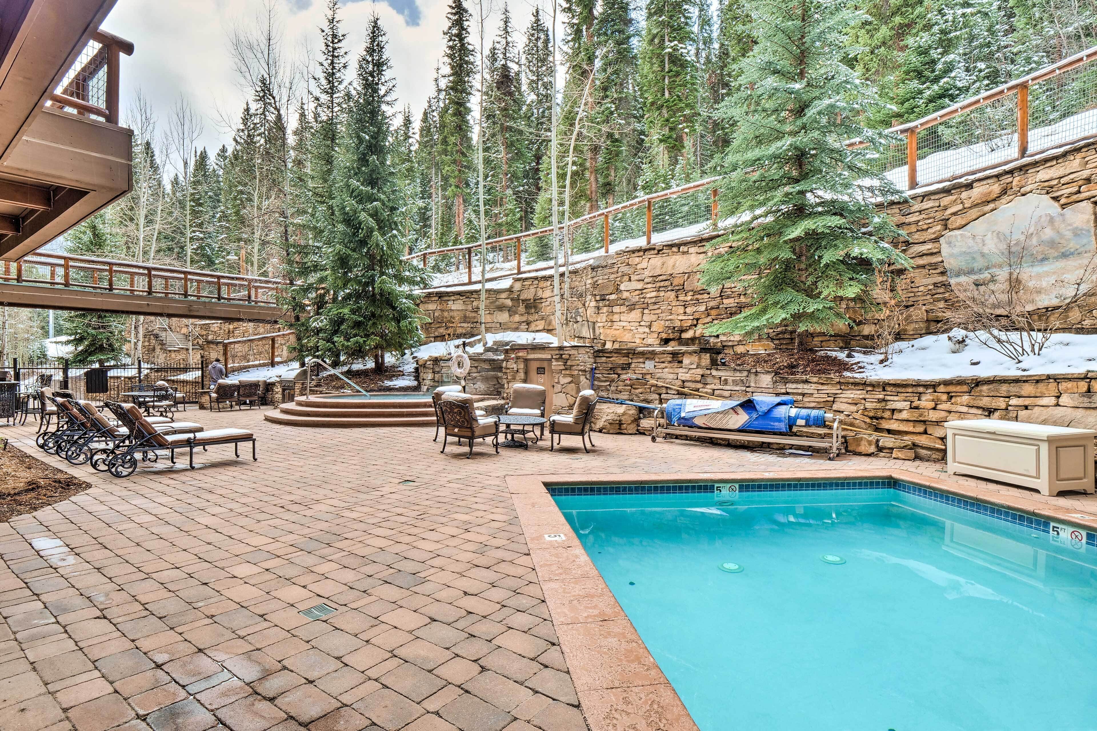 A pool area with lounge chairs, a stone wall, and a wooden deck.