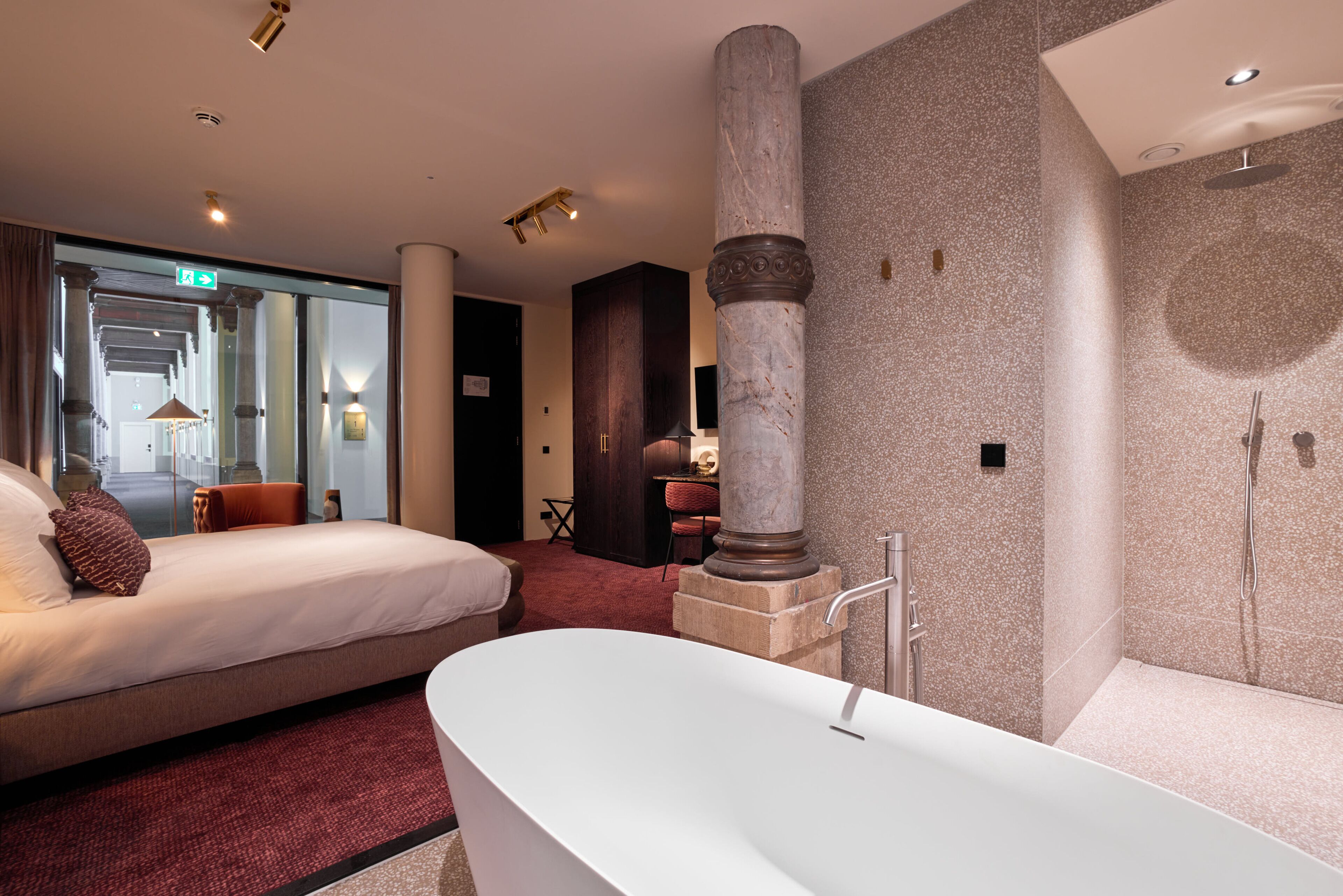 Una habitación de hotel moderna con una cama grande, una zona de estar separada, una bañera y una ducha.