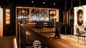 A bar area with a wooden counter, black bar stools, and a wine rack in the background. - Heavens Hotel (Hoorn)