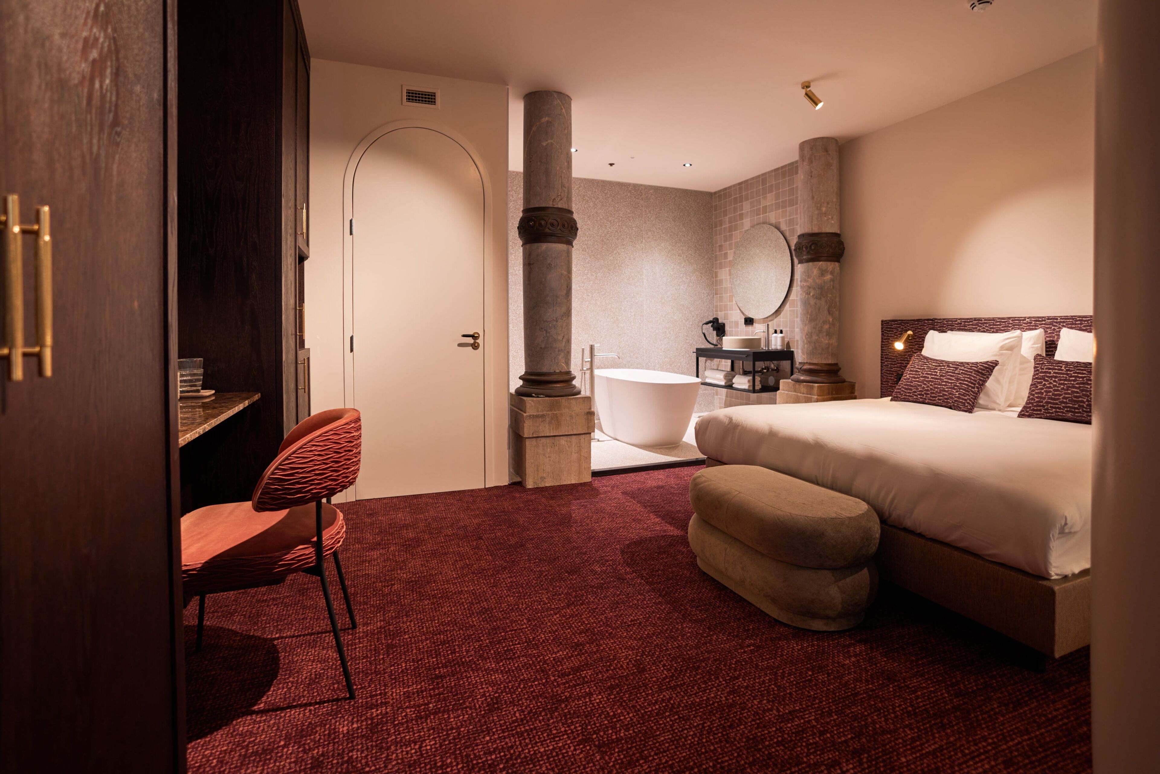 A hotel room with a bed, a desk, a chair, a bathtub, and a large mirror.