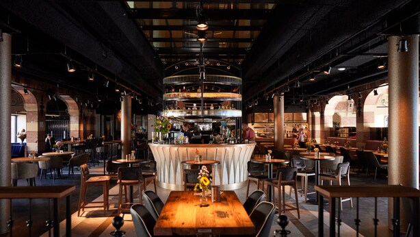 A restaurant with a central bar, multiple tables, and chairs. - Heavens Hotel (Hoorn)