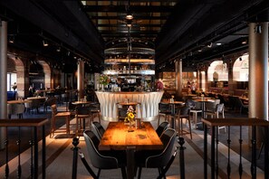 A restaurant with a central bar, multiple tables, and chairs. - Heavens Hotel (Hoorn)