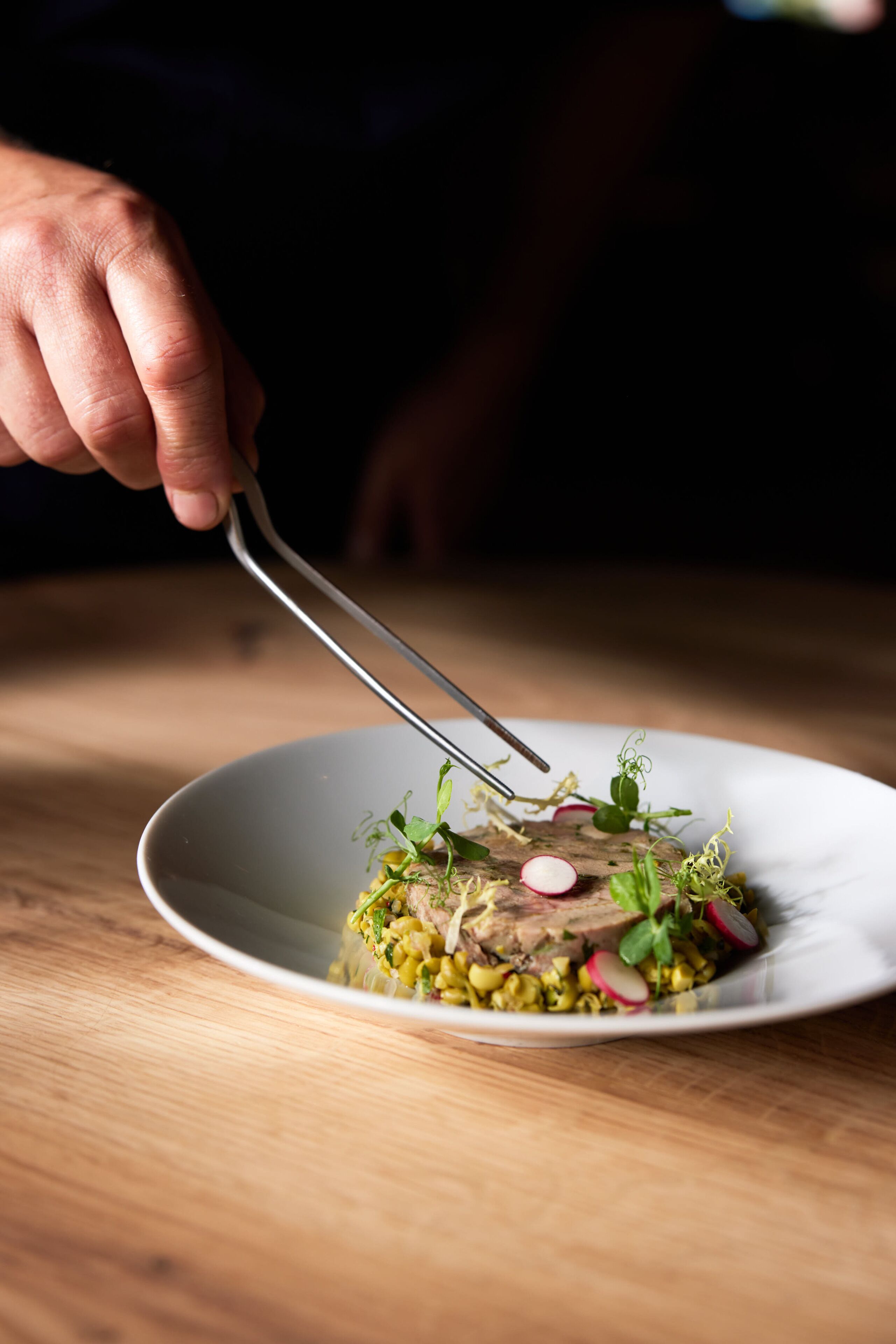 Une personne utilise des pinces pour servir un plat dans une assiette blanche.