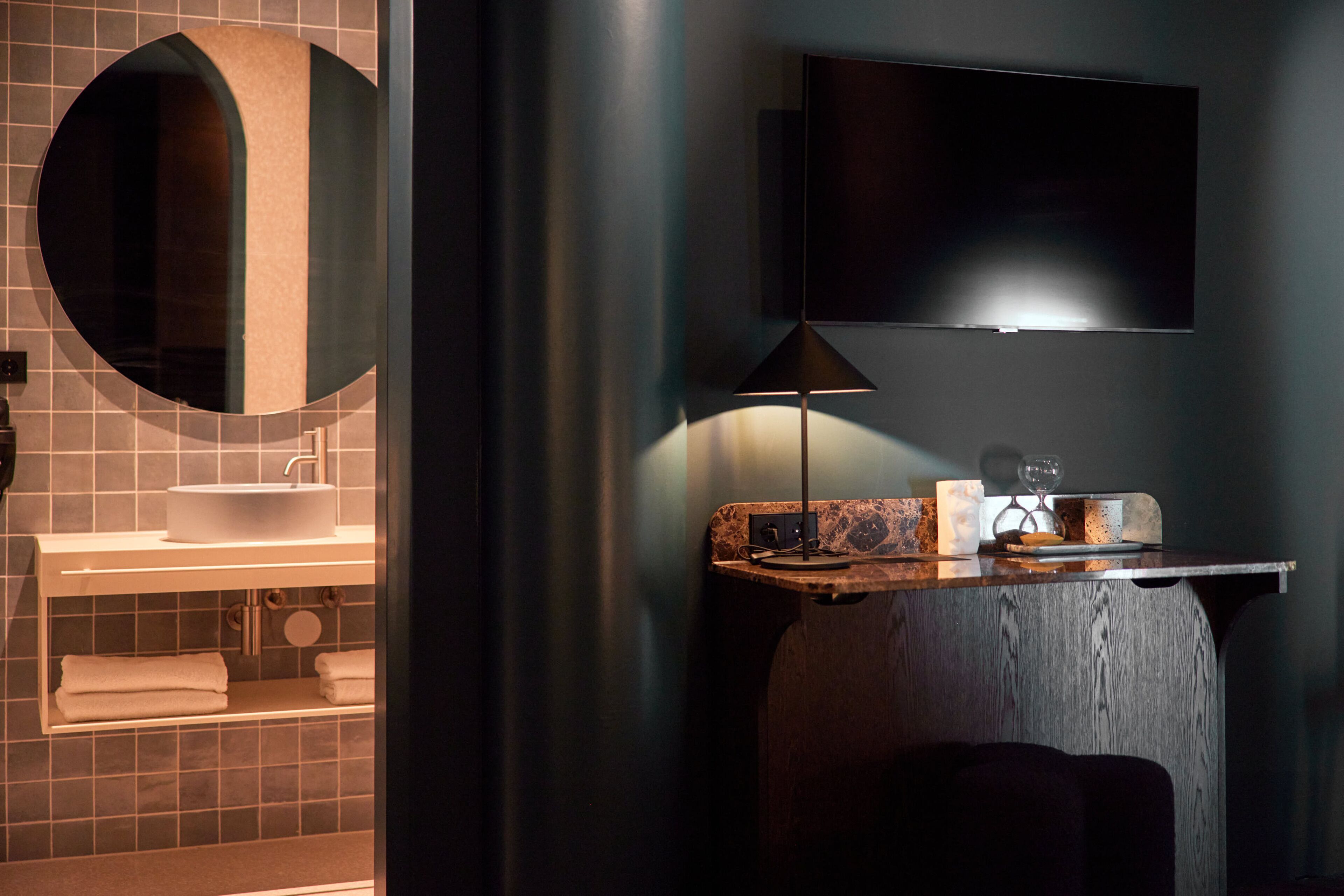 A modern bathroom with a round mirror, a sink, a television mounted on the wall, and a wooden vanity.
