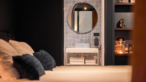 A modern bedroom with a bed, a round mirror, a white sink, and a shelf with decorative items. - Heavens Hotel (Hoorn)