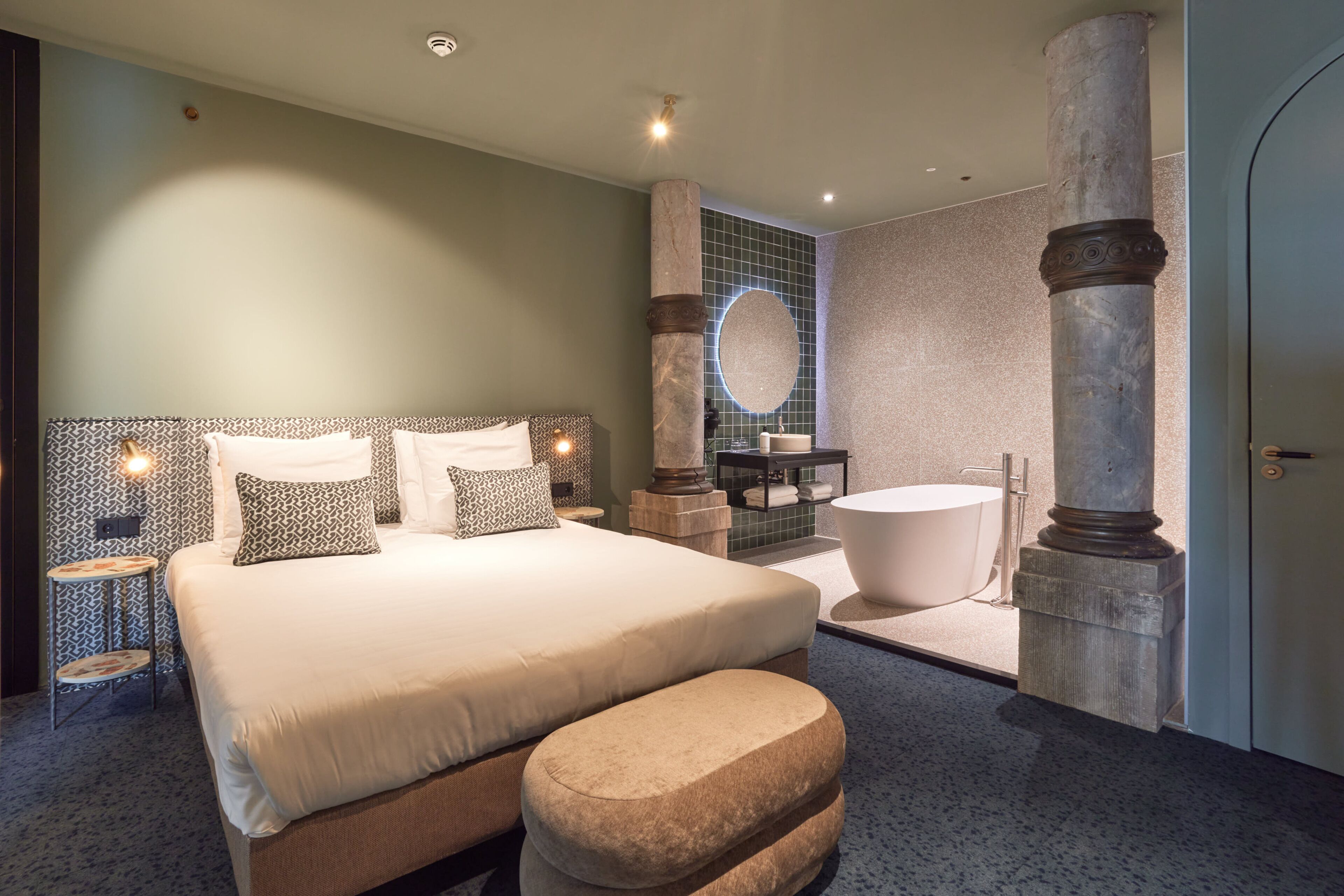 Een moderne hotelkamer met een groot bed, een zithoek, een badkuip en een marmeren pilaar.