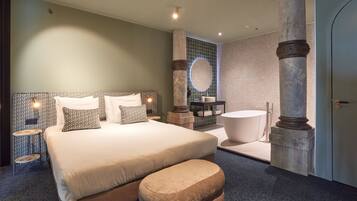 Een moderne hotelkamer met een groot bed, een zithoek, een badkuip en een marmeren pilaar.