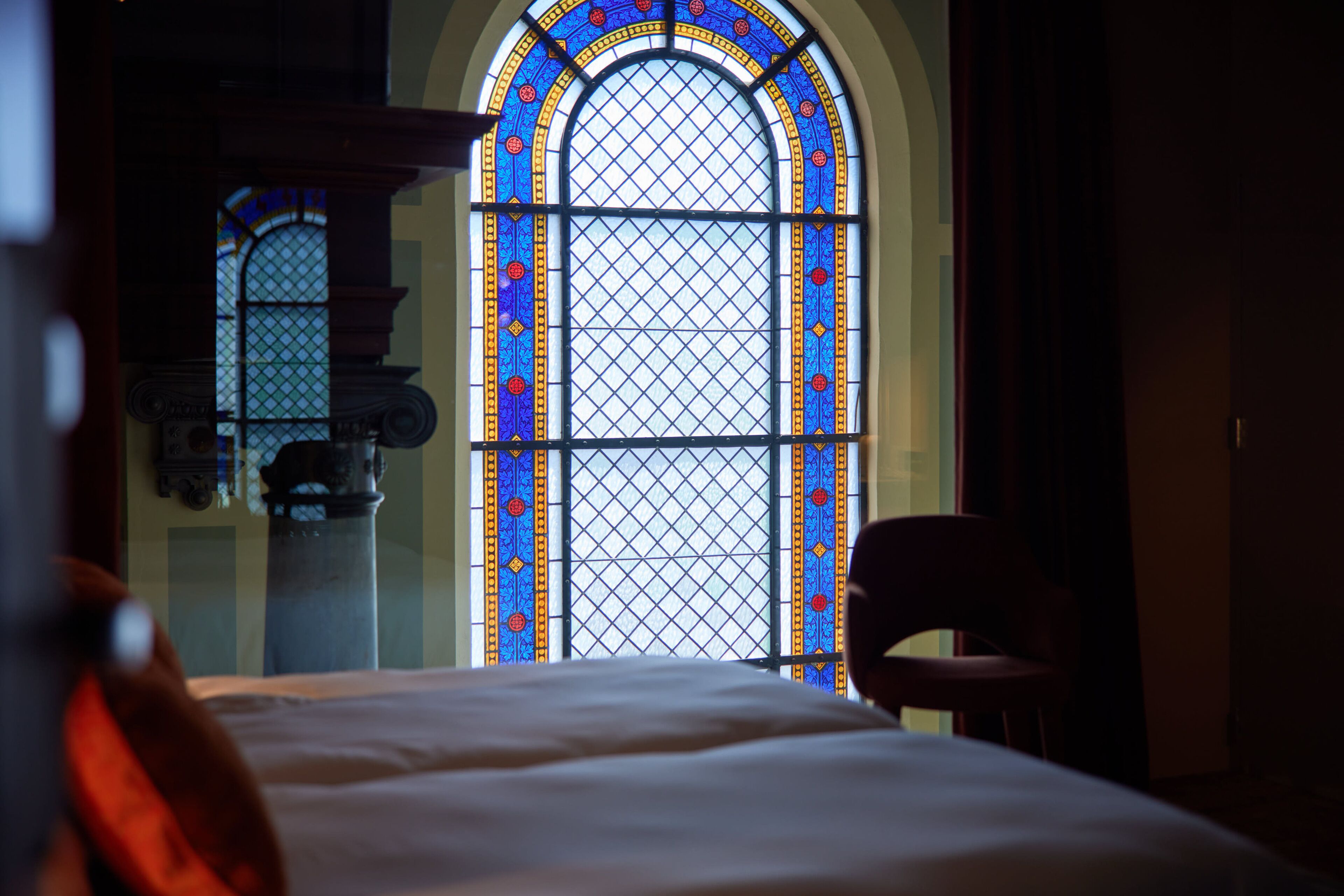 A room with a large stained glass window, a bed, and a chair.