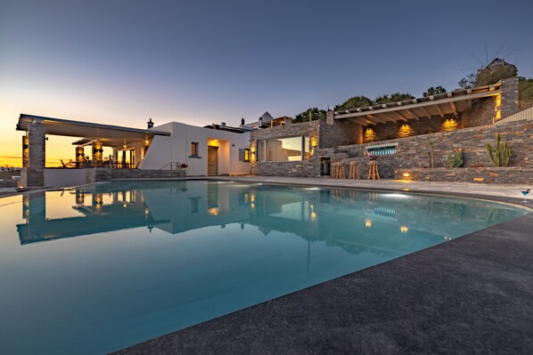 A modern house with a swimming pool, stone walls, and outdoor lighting.