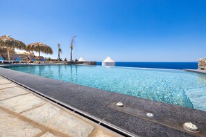 A pool with clear blue water, a stone deck, and a view of the ocean.
