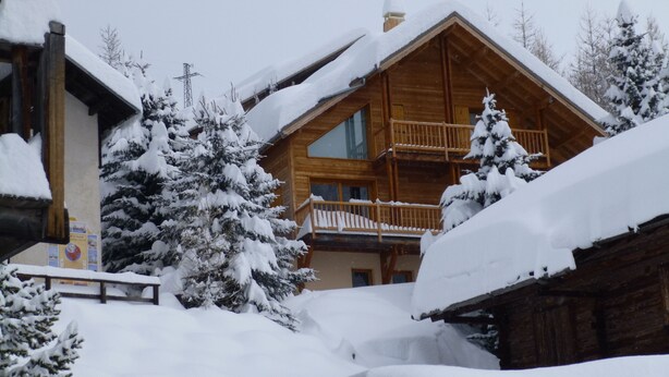 Un chalet en bois doté d’un balcon, entouré d’arbres couverts de neige.
