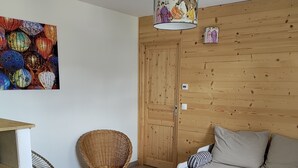Un salon chaleureux avec un mur en bois, un canapé, un fauteuil en osier, une petite table avec un livre et une lanterne colorée servant de décoration.