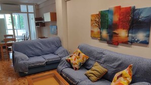 Una sala de estar con un sofá azul, una mesa de centro de madera y una pared decorada con cuadros de colores.