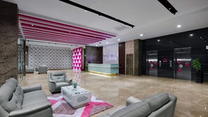 Un hall d’hôtel moderne comprenant un comptoir d’accueil, un espace salon et des ascenseurs.