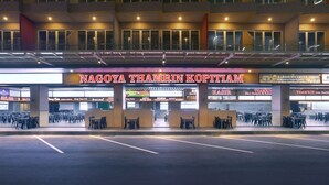 Un bâtiment sur lequel est apposée une enseigne indiquant « NAGOYA THAMRIN KOPITIAM », et qui dispose de plusieurs espaces aménagés avec des tables et des chaises.