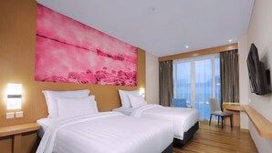 Une chambre d’hôtel avec deux lits, une grande œuvre d’art rose accrochée au mur, un téléviseur fixé au mur et une vue sur la ville à travers de grandes fenêtres.