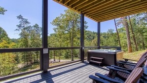 Une terrasse en bois dotée d’un jacuzzi, d’un espace salon et offrant une vue sur un paysage boisé.