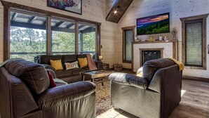 Un salon chaleureux avec des canapés en cuir, une cheminée et de grandes fenêtres donnant sur une forêt.