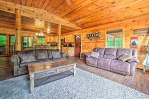 A cozy cabin interior with wooden walls, a kitchen area, and two sofas.