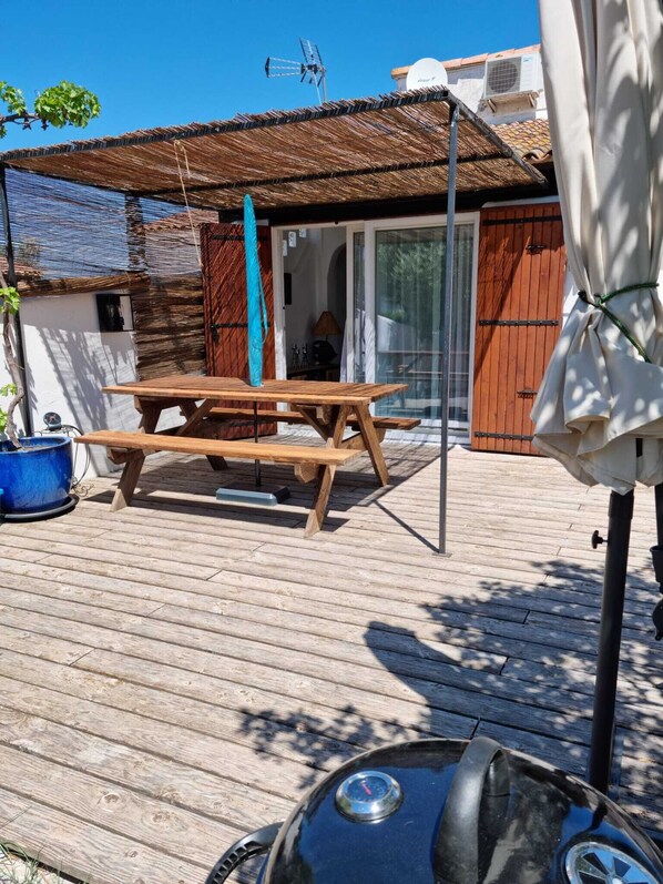 A wooden deck with a picnic table, a barbecue grill, and a covered umbrella.