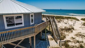 A beach house with a wooden deck and a staircase leading to a sandy beach.