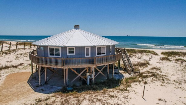 A beach house with a circular structure, a wooden deck, and a staircase leading to a second level.