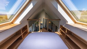 A bedroom with a sloped ceiling, skylights, wooden shelves, and a bed. - The Byre, Waternish, Isle of Skye - Luxury Self Catering (Isle of Skye)