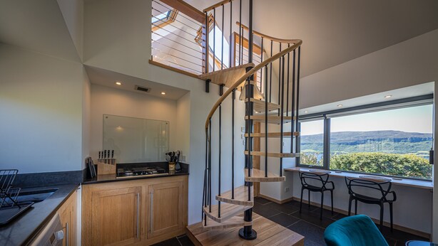A modern kitchen with a wooden staircase, a large window with a view of the countryside, and a seating area with chairs. - The Byre, Waternish, Isle of Skye - Luxury Self Catering (Isle of Skye)