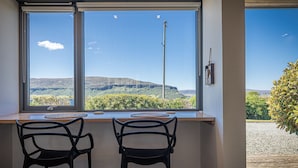 A room with two black chairs at a wooden table by a large window with a view of a hilly landscape. - The Byre, Waternish, Isle of Skye - Luxury Self Catering (Isle of Skye)