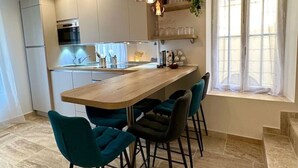 Una cocina moderna con una isla central, taburetes de bar y un ventanal con cortinas.