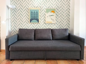 A grey sofa in a room with a chevron-patterned wallpaper and two framed pictures on the wall.