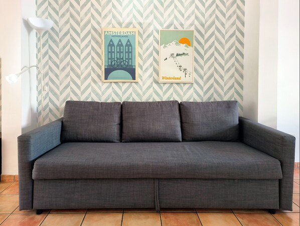 Un canapé gris dans une pièce dont le papier peint présente un motif en chevrons, et où deux tableaux encadrés sont accrochés au mur.