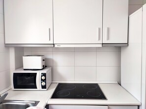 A compact kitchen with white cabinets, a microwave, a toaster, and an induction cooktop.