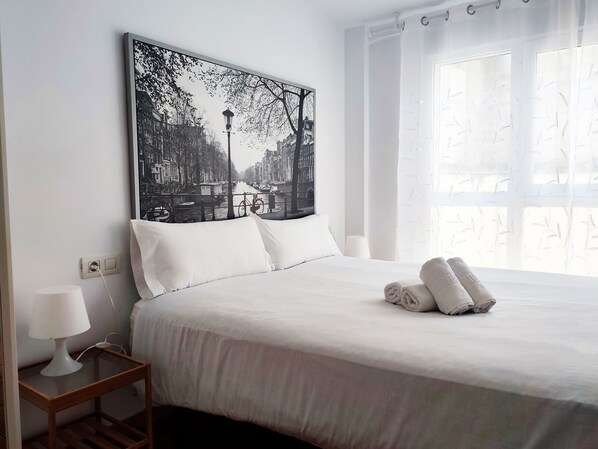 A neatly made bed with white linens and a rolled towel, a bedside table with a lamp, and a large black and white cityscape painting on the wall. - Flats Friends Nave 1 bedroom with terrace (Valencia)