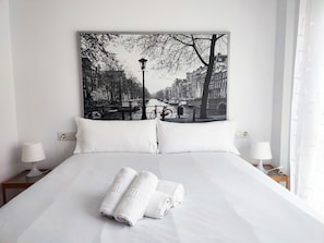 A hotel room with a large bed, white bedding, two bedside lamps, and a cityscape artwork on the wall. - Flats Friends Nave 1  bedroom with terrace (Valencia)