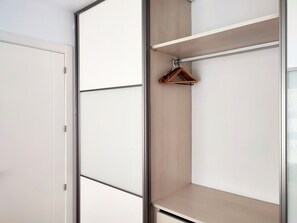Un dressing accessible sans porte, doté d’une armoire à portes miroir, d’étagères en bois et d’une tringle pour suspendre les vêtements.