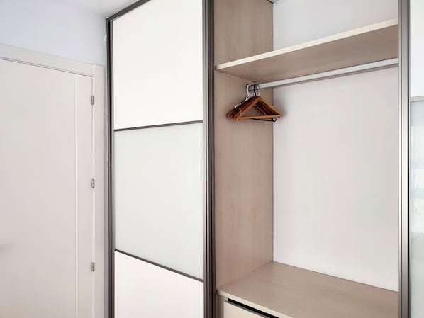 A walk-in closet with a mirrored wardrobe, wooden shelves, and a hanging rack.