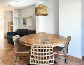 A dining area with a round wooden table surrounded by wicker chairs, a woven pendant light, and a sofa against a wall with patterned wallpaper. - Flats Friends Nave 1  bedroom with terrace (Valencia)
